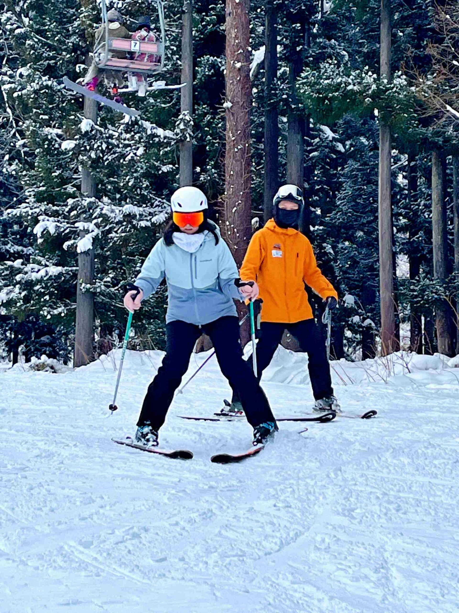 滑雪教練穿著橘色雪衣在學員身後進行近距離雙板（SKI）滑行姿勢與動作矯正指導